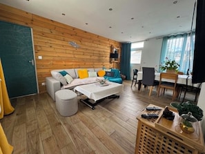 A room with a wooden wall, a sofa, a dining table, and a small table with a plant.