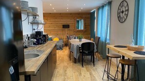 Una cocina moderna con suelo de madera, un comedor con mesa y sillas, y un gran reloj de pared.