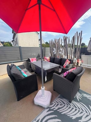 An outdoor seating area with wicker furniture, a red umbrella, and a patterned rug.