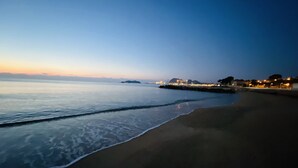 Uma praia com águas calmas e uma paisagem urbana distante ao anoitecer.