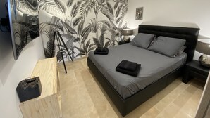 Quarto com cama, mesa de cabeceira, luminária, espelho e planta.