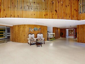 A modern lobby with wooden paneling, a reception desk, two plush armchairs, and a glass display case. - Radisson Hotel Bareilly Airport (Bareilly)