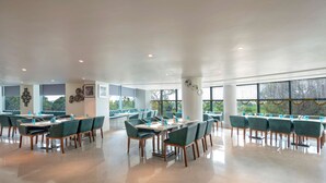 A spacious dining area with multiple tables and chairs, large windows, and a clean, modern design. - Radisson Hotel Bareilly Airport (Bareilly)