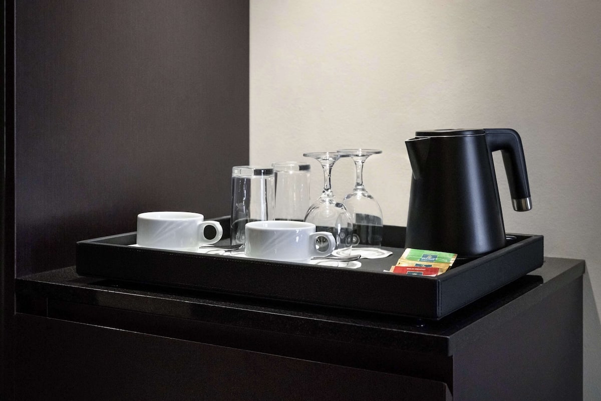 A black tray with a coffee maker, two white cups, two glass tumblers, and a packet of sugar.