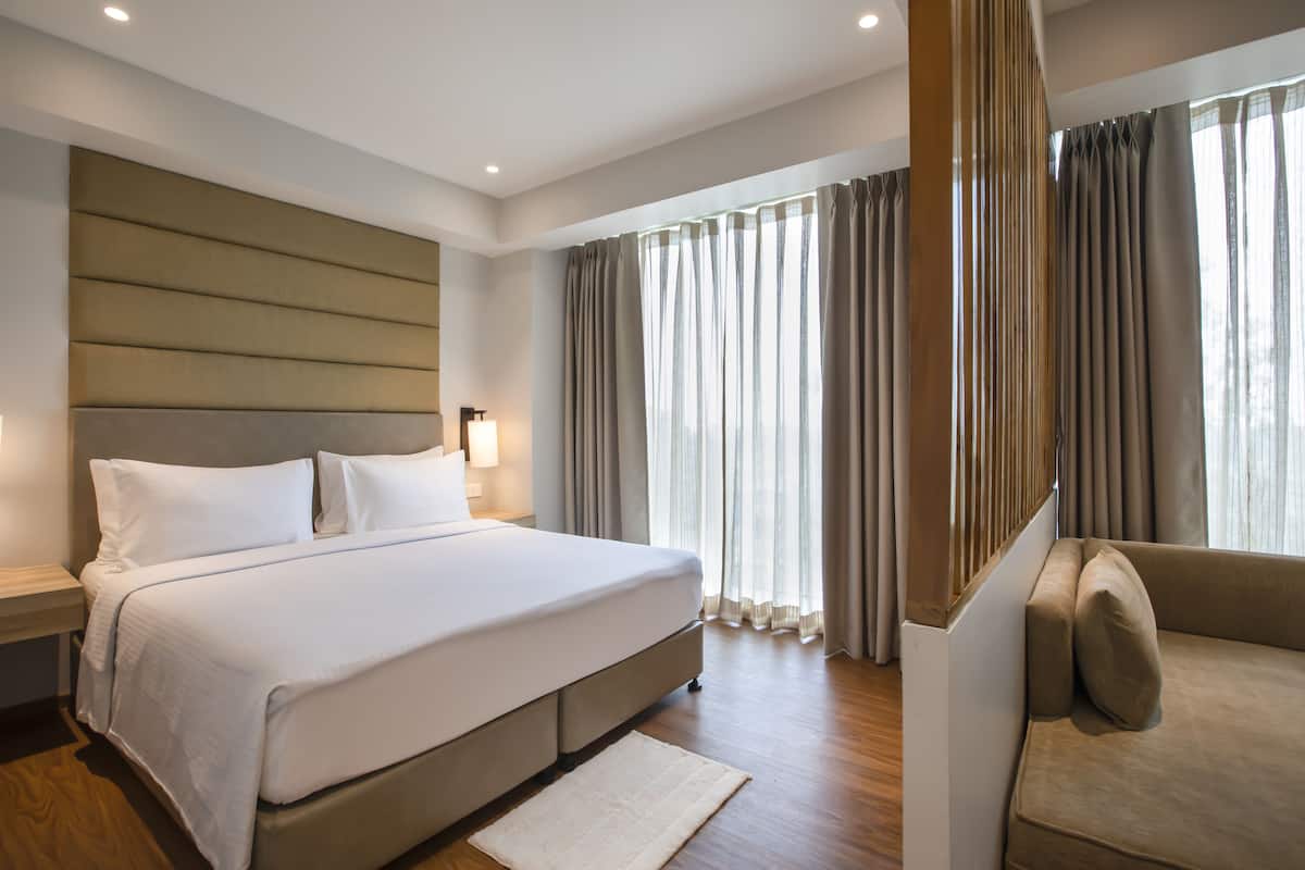 A modern hotel room with a large bed, a sofa, and curtains.