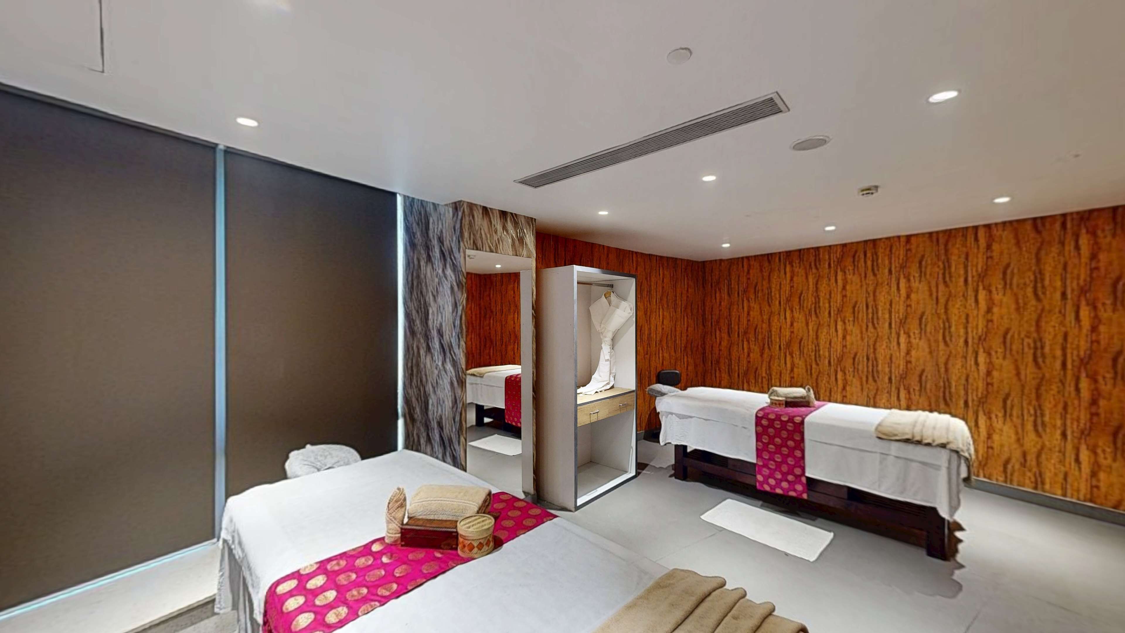 A modern hotel room with a large bed, a separate seating area, a vanity with a mirror, and a wooden accent wall.