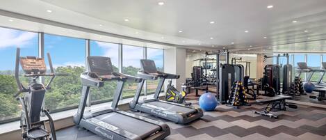 A gym with treadmills, elliptical machines, and weightlifting equipment, large windows, and a chevron-patterned floor.
