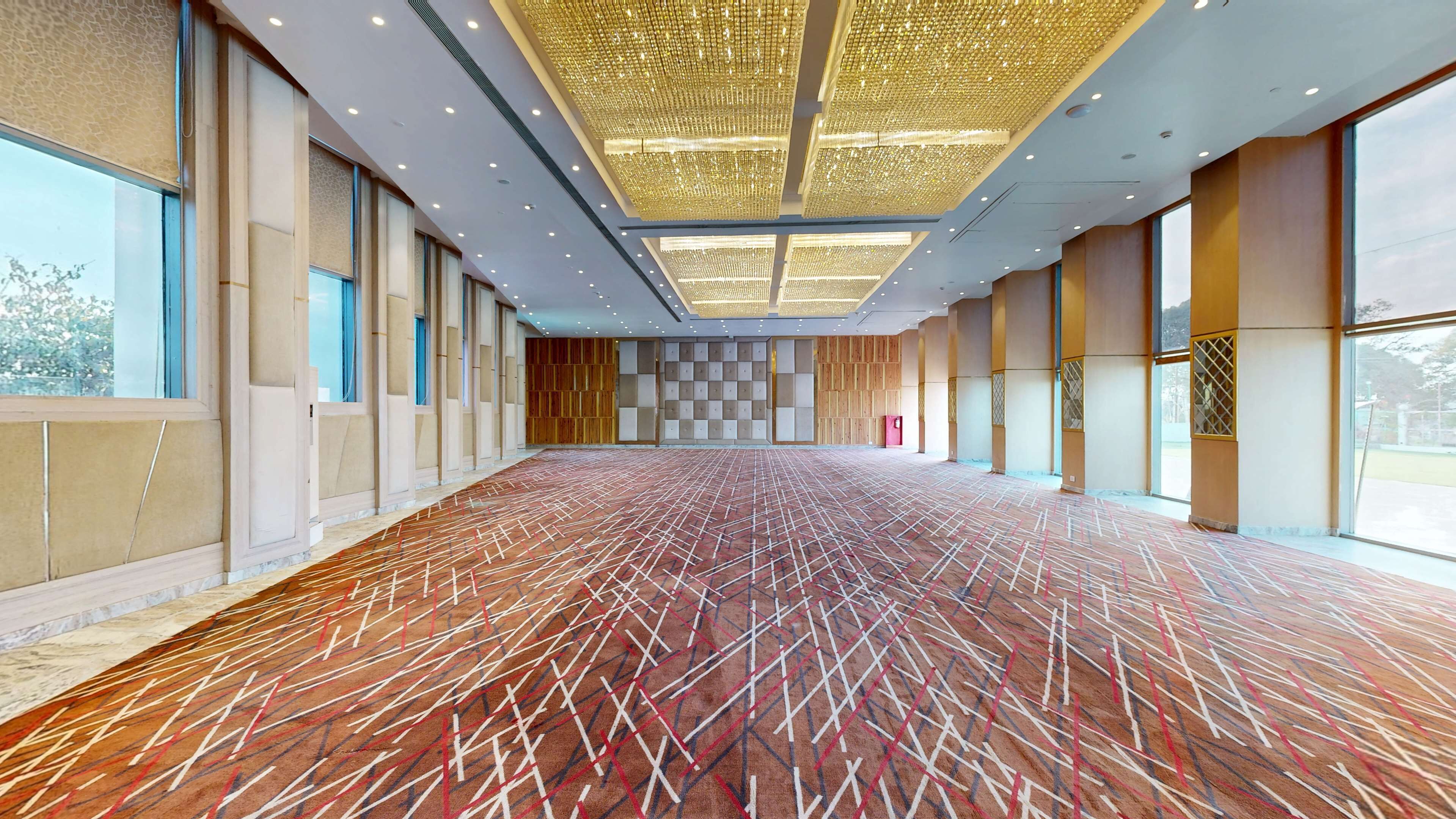 A spacious, well-lit hall with patterned carpet, large windows, and a modern ceiling design.