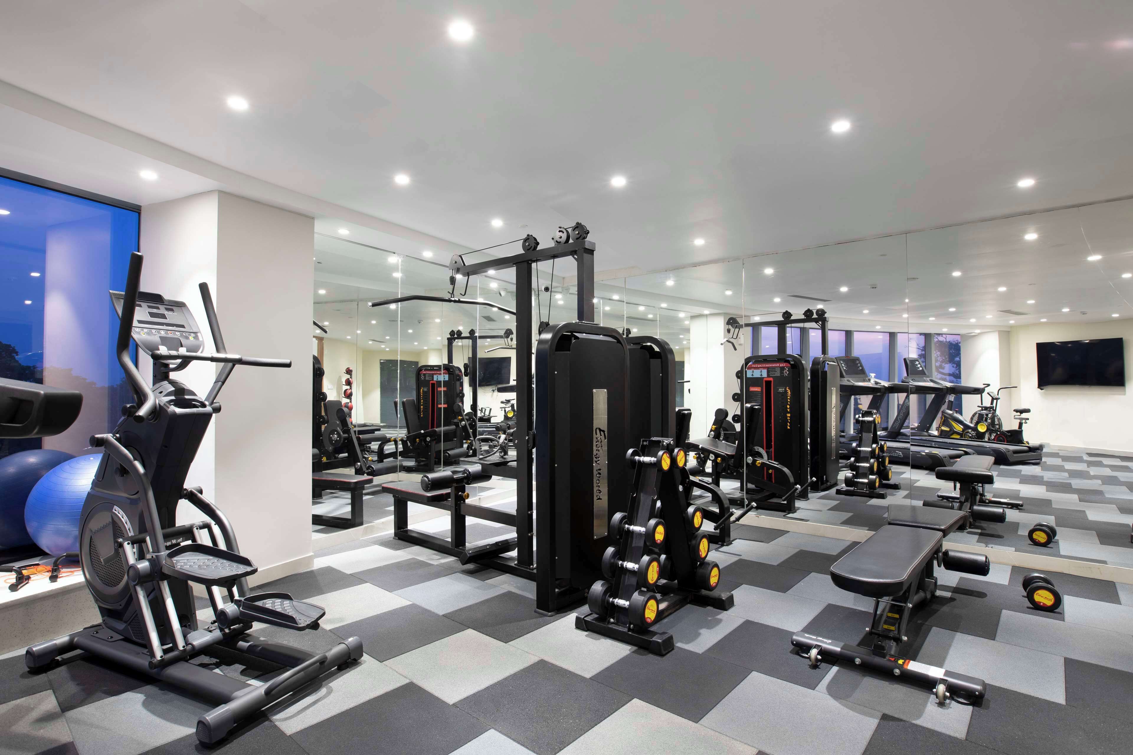 Un gimnasio moderno con diversos equipos de ejercicio, paredes espejadas y suelo a cuadros.