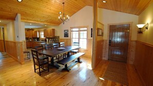 A spacious dining area with a wooden table and benches, a kitchen in the background, and a wooden door.