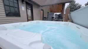 A hot tub with a wooden deck and a house in the background.