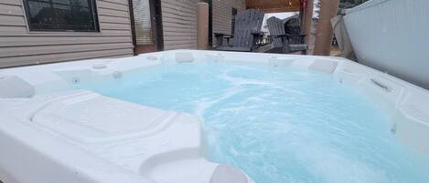 Un jacuzzi con un muelle de madera y una casa al fondo.