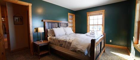 A bedroom with a wooden bed, a nightstand, a lamp, and a window.