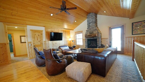 A cozy living room with a stone fireplace, leather sofas, and a ceiling fan.