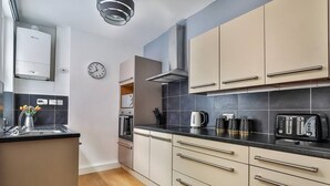 Une cuisine moderne avec des armoires de couleur beige, un plan de travail noir et un four encastré.