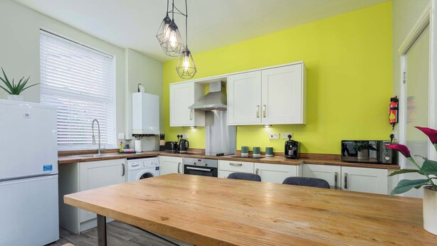Una cocina funcional con armarios blancos, una mesa de madera y una lámpara colgante moderna.