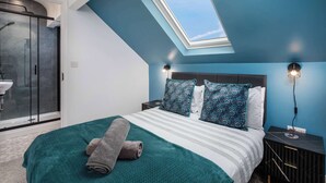 Un dormitorio con tragaluz, cama con ropa de cama color aguamarina y mesita de noche con lámpara.