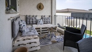 Een balkon met een zachte zithoek, een rieten stoel en een tafeltje.