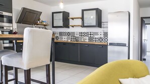 Een moderne keuken met een eethoek, voorzien van een barstoel, een gele bank en een decoratieve spatwand.