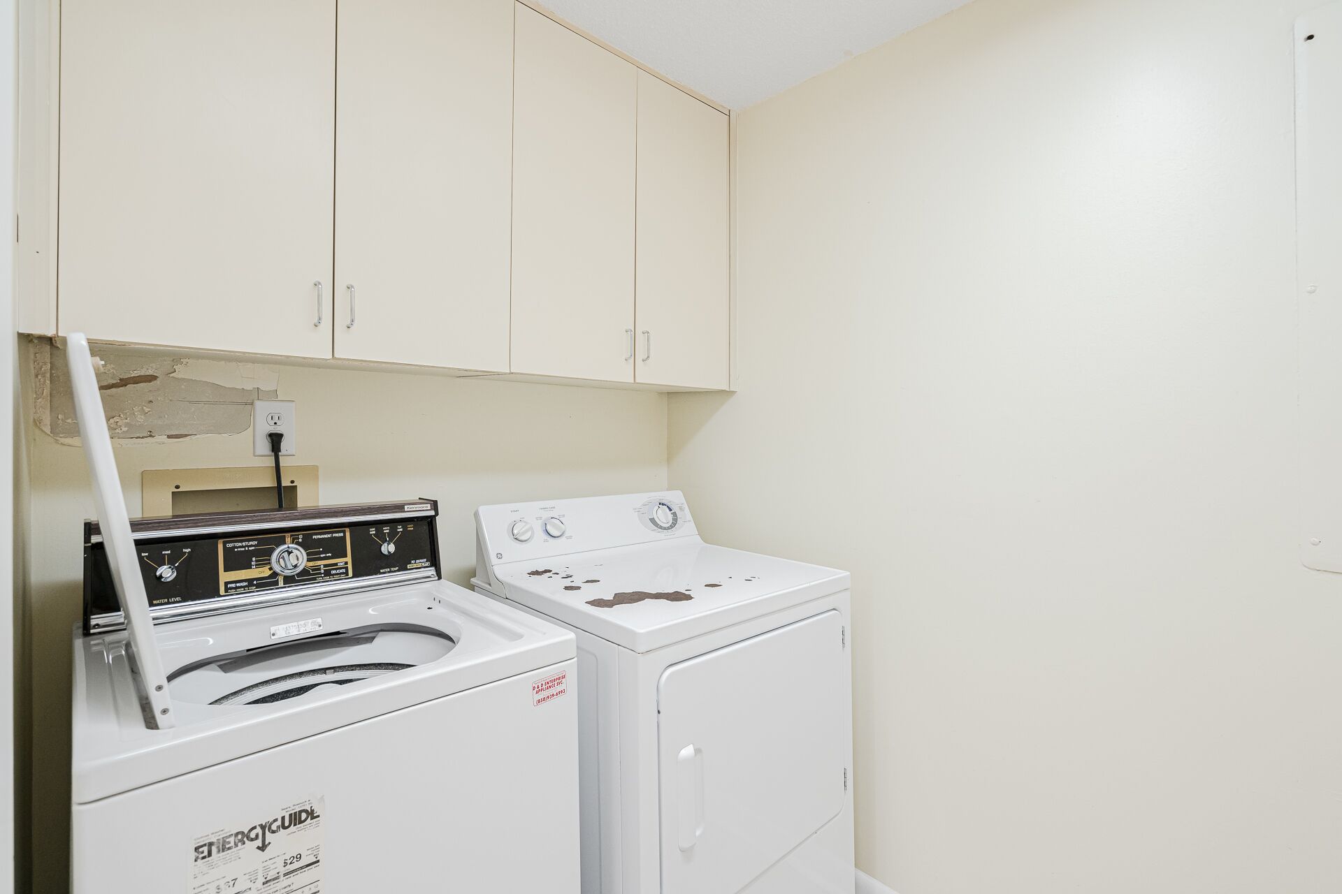 A laundry room with a front-loading washer and dryer, a water heater, and cabinets above.