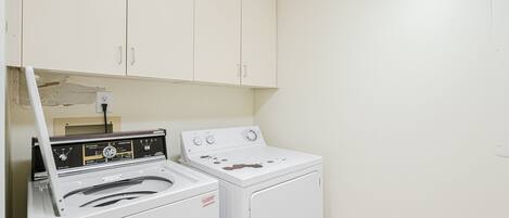 A laundry room with a front-loading washer and dryer, a water heater, and cabinets above.