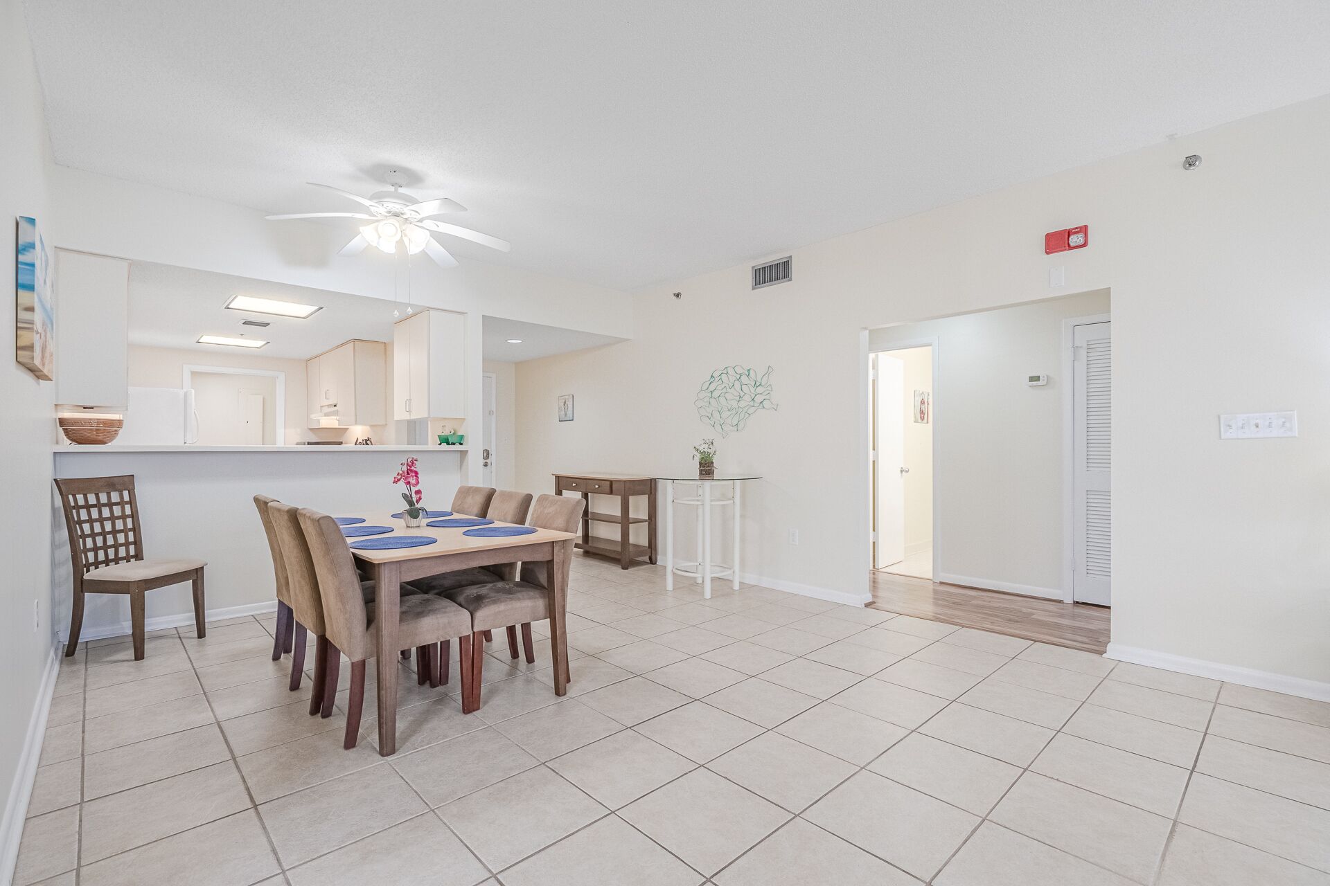 A dining area with a wooden table and chairs, a kitchen in the background, and a ceiling fan.