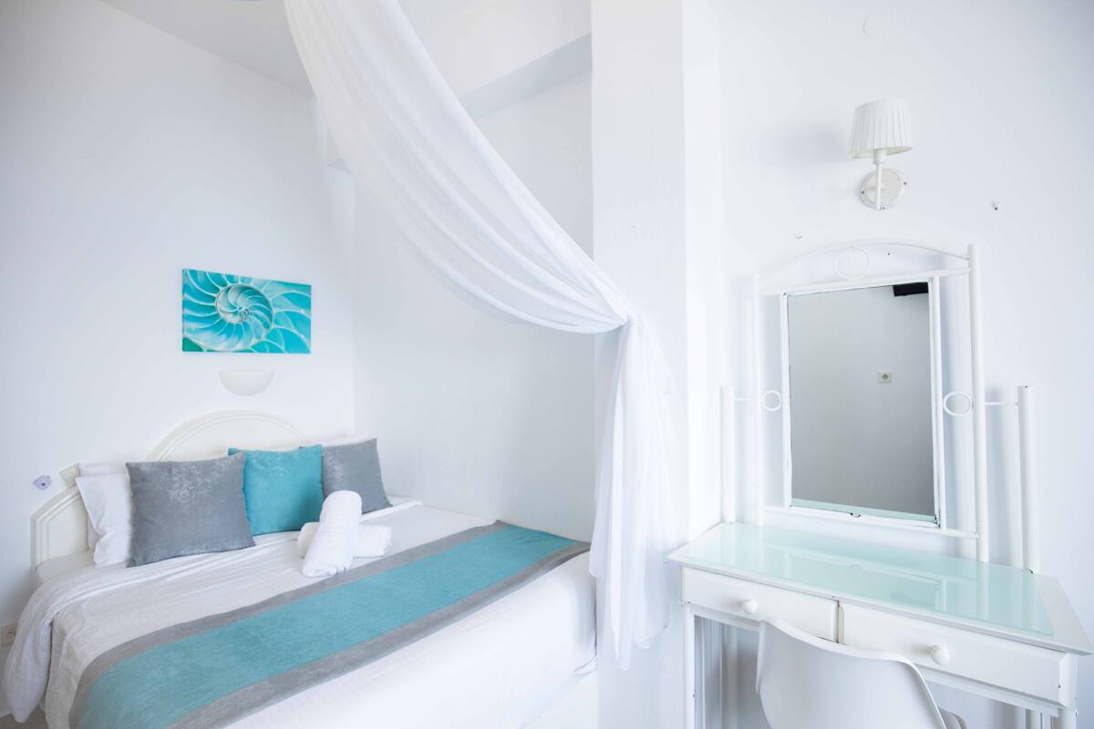 A bedroom with a bed, a vanity with a mirror, and a wall-mounted light fixture.