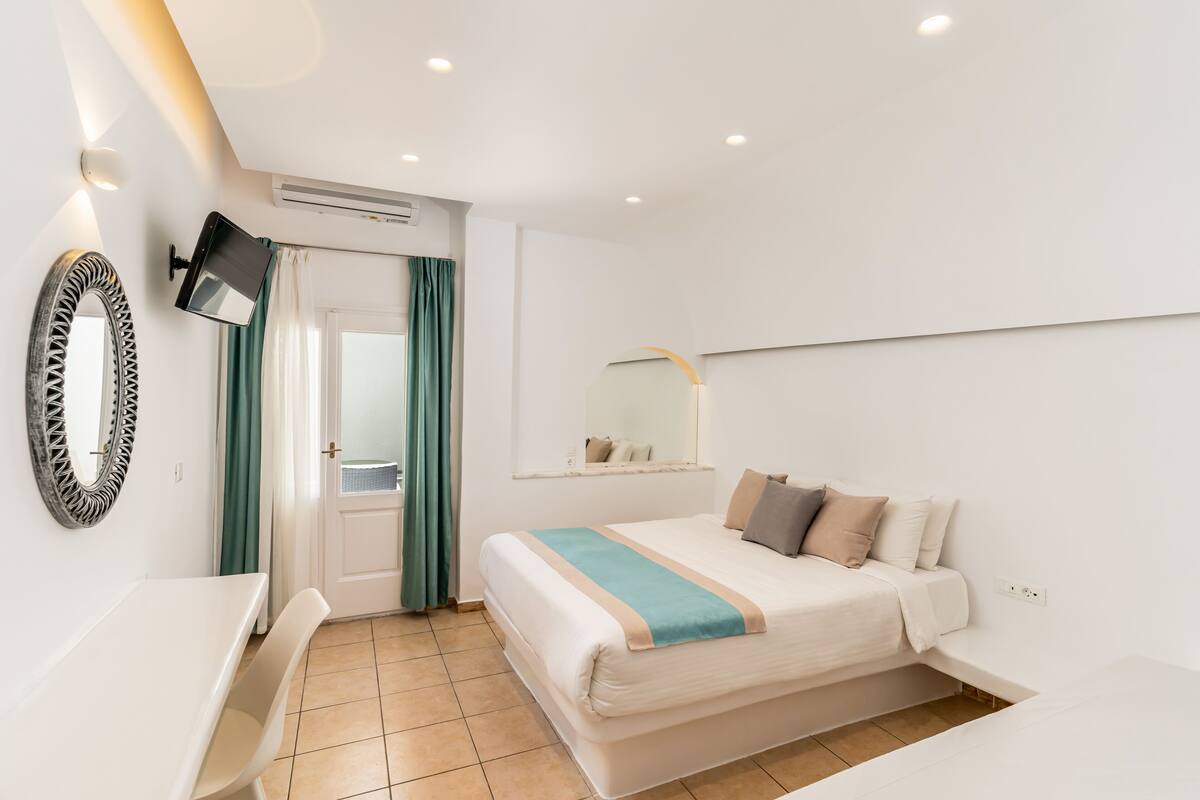 A modern hotel room with a bed, a desk, a mirror, and a TV.