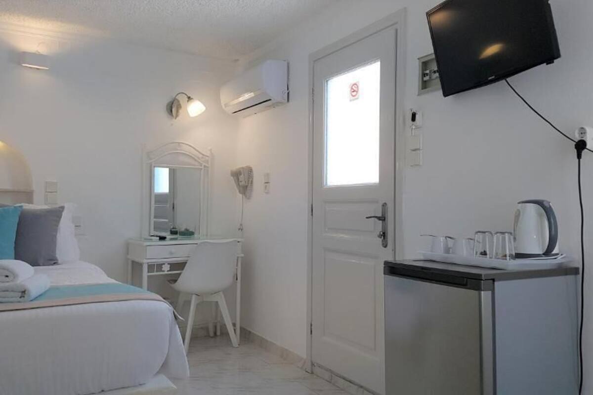 A hotel room with a bed, a desk, a chair, a television, and a kitchenette.