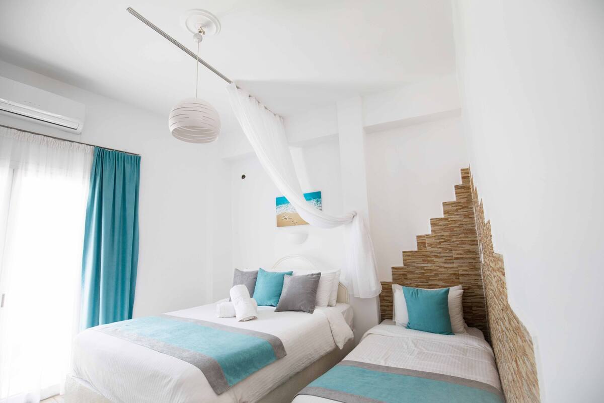 A hotel room with two beds, a staircase, a ceiling fan, and a beach-themed artwork.
