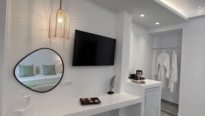 Un baño moderno con tocador blanco, televisor montado, toallero y un taburete pequeño.