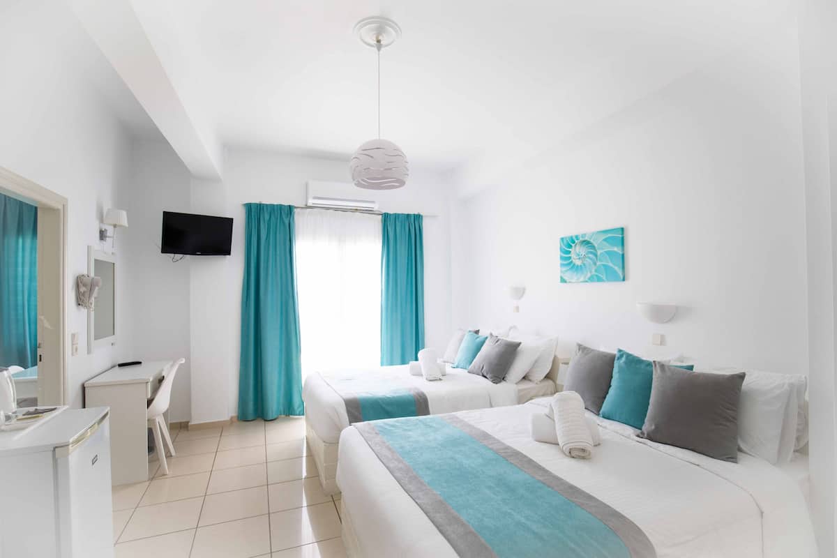 A hotel room with two beds, a desk, a TV, and a window with curtains.