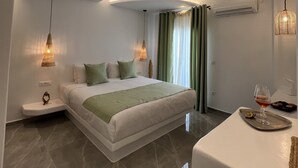 Una habitación de hotel moderna con techo curvo, una cama grande con ropa de cama verde, una mesita de noche con una copa de vino y una pequeña estatua.