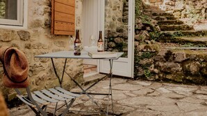 Ein Steinhaus mit rustikalem Inneren, ein Tisch mit Flaschen, ein gewebter Korb und ein Metallstuhl.