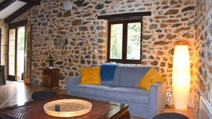Ein Zimmer mit Steinwänden, einer grauen Couch, einem Holztisch mit Tablett und einer hohen Stehlampe.