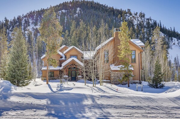 Escape to a serene mountain retreat with a symmetrical log cabin-style hotel, nestled among evergreen trees and snow-covered peaks.