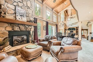 A spacious living room with a stone fireplace, leather furniture, and large windows offering natural light. - Keystone Gulch 1688 5 Bedroom Estate by RedAwning (Keystone)