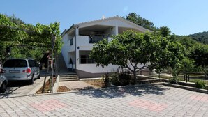 A two-story building with a flat roof, a balcony on the second floor, and a paved driveway with a tree in front. - Lovely 2-bedroom Apartment in Poljica (Marina)