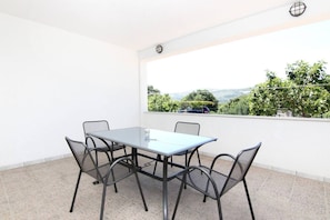 Un balcón con mesa y cuatro sillas, vistas a zonas verdes y colinas, y una pared blanca.