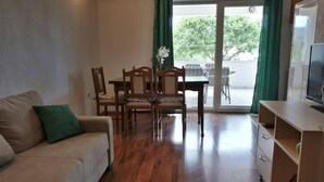 A living room with a sofa, a dining table with chairs, a TV, and a sliding glass door leading to an outdoor area. - Lovely 2-bedroom Apartment in Poljica (Marina)