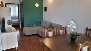 A living room with a wooden dining table, a sofa, and a small kitchen area with a refrigerator. - Lovely 2-bedroom Apartment in Poljica (Marina)