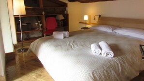 A hotel room with a wooden ceiling, a bed with white linens, a red chair, a desk with a lamp, and a shelf with various items. - Arias la Suite del Duomo - Sea View Terrace (Cefalù)