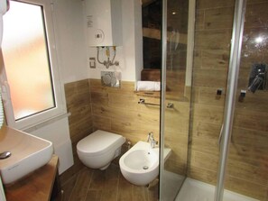Un baño con inodoro, bidé y lavamanos, baldosas de madera en la pared y una cabina de ducha de vidrio.