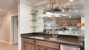 A kitchen with a granite countertop, wooden cabinets, and a glass display shelf above the sink. - New to the Rental Market, Newly Owner, Newly Renovated!!! (Orange Beach)