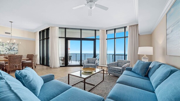 A spacious living room with a large sofa set, a coffee table, and a dining area with wicker furniture. There is a balcony with a view of the ocean. - New to the Rental Market, Newly Owner, Newly Renovated!!! (Orange Beach)