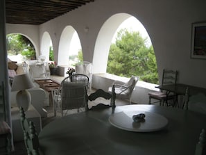 A spacious patio with white furniture, a round table, and arched windows overlooking greenery.