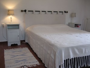 A bedroom with a white bed, a bedside table with a lamp, and a nightstand.