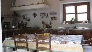 Een keuken met een eettafel voor vier personen, een raam met gordijnen, en diverse keukengerei en apparaten.