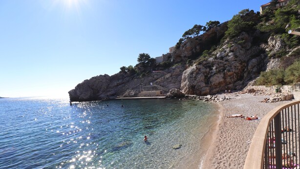 A beach with clear water, rocky cliffs, and a few people sunbathing. - Art Apartment Nearby the sea (Dubrovnik)