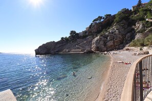 A beach with clear water, rocky cliffs, and a few people sunbathing. - Art Apartment Nearby the sea (Dubrovnik)